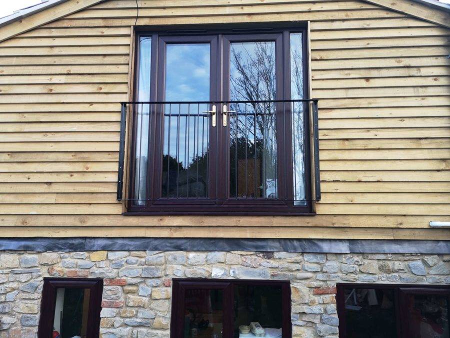 Timber clad home extension with dark framed French doors and stonework below